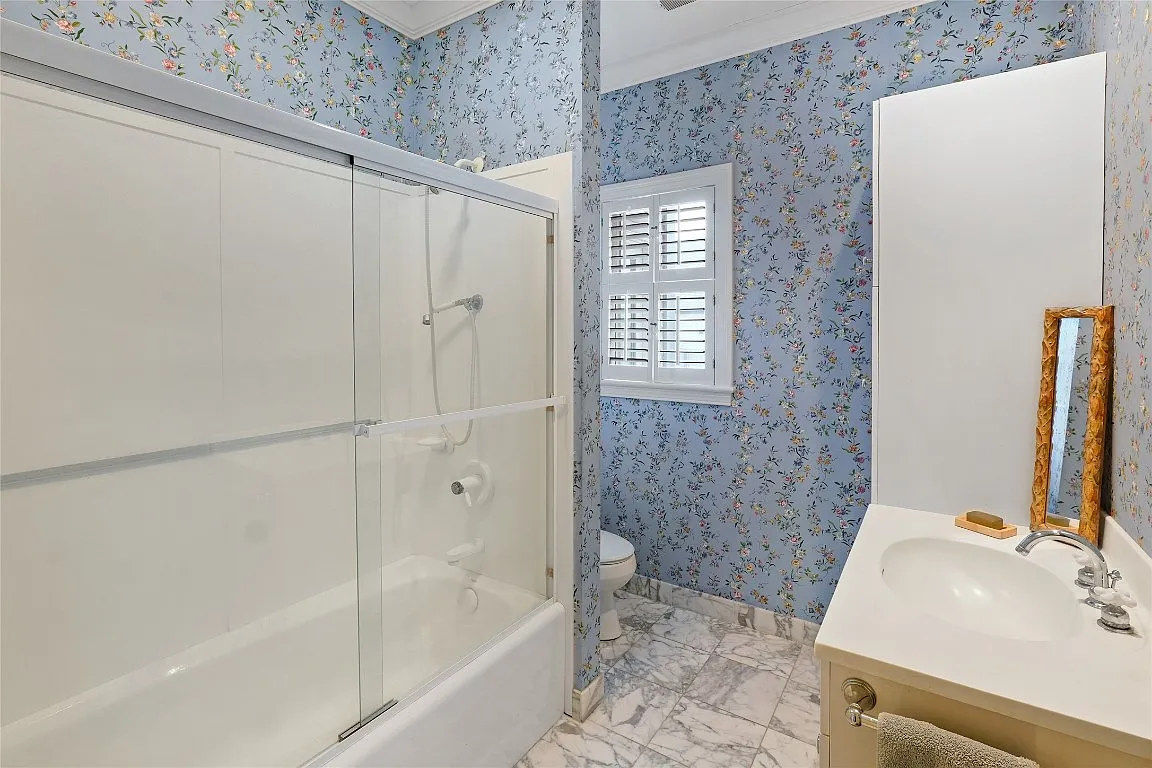 The bath before: blue floral wallpaper and a tub behind sliding glass.