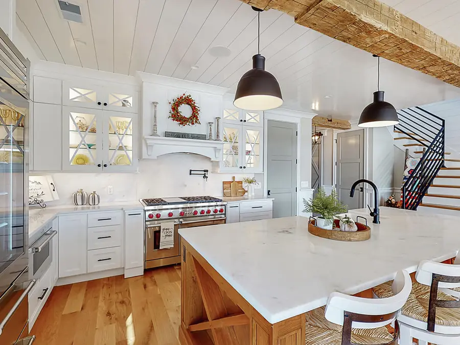 White farmhouse kitchen with marble island, wood beam ceiling and black pendant lights