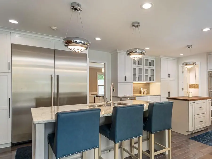 White kitchen with built-in refrigerator, granite island and blue upholstered bar stools