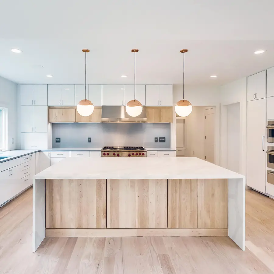 White kitchen with light wood island, waterfall stone countertop and globe pendants