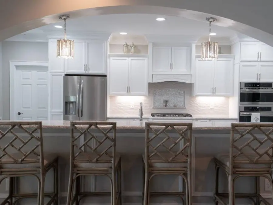 White kitchen seen through an archway with crystal pendants and lattice-back bar stools