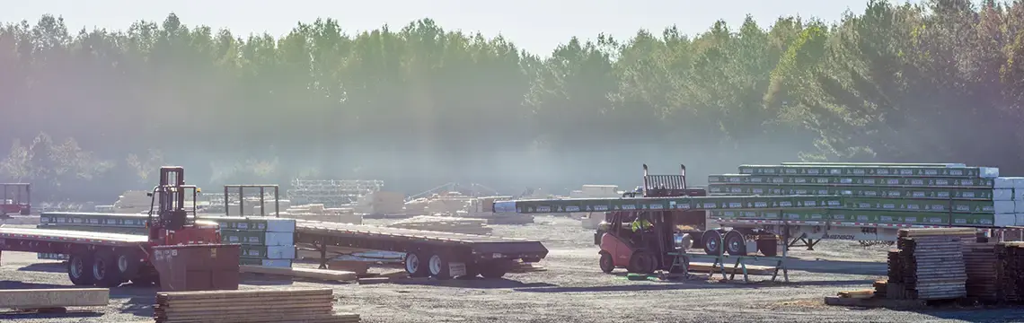 Hazy lumber yard with forklifts and flatbed trailers loaded with wrapped materials