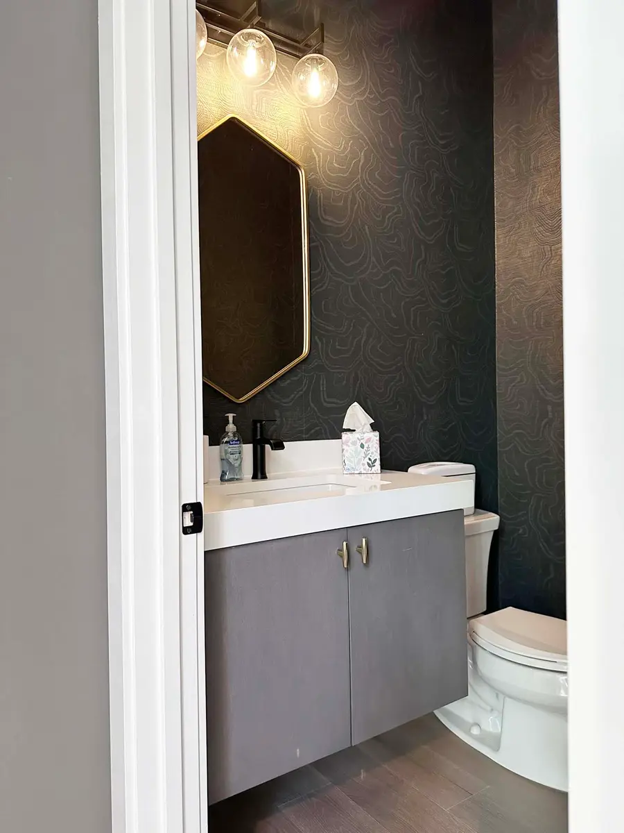 Powder room with floating gray vanity, brass hexagon mirror and dark patterned wallpaper