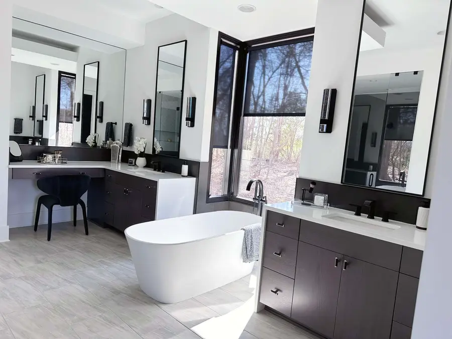 Primary bath with freestanding tub, dark wood vanities, makeup desk and corner windows