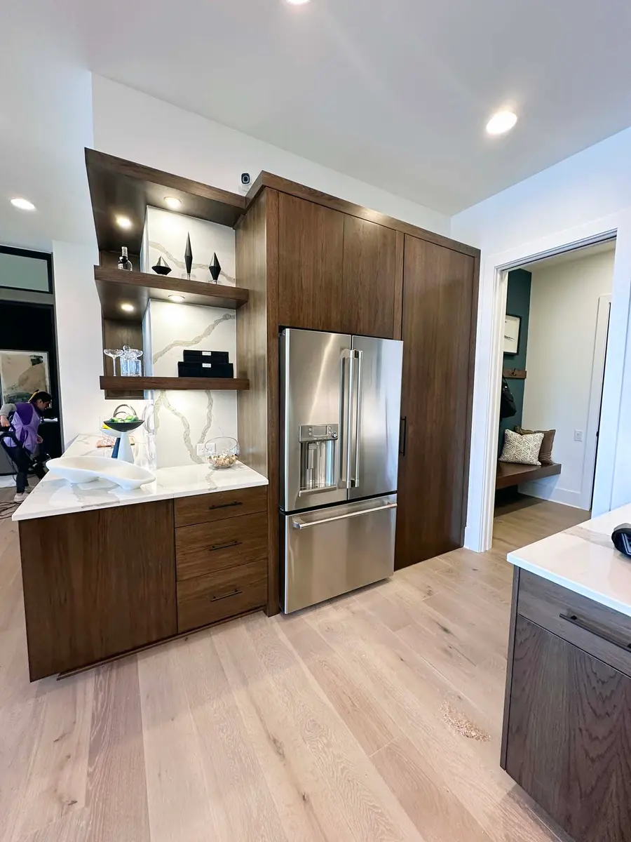 Wood cabinet wall with built-in refrigerator, lit open shelves and marble-look backsplash