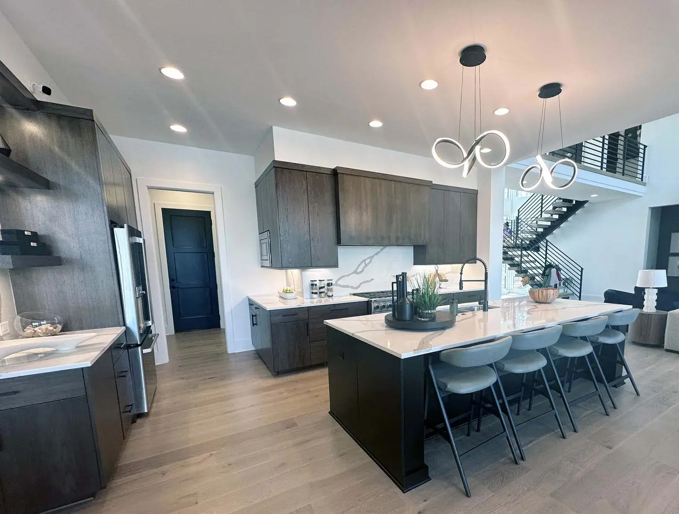 Kitchen with dark wood cabinets, white stone island, gray stools and loop pendants
