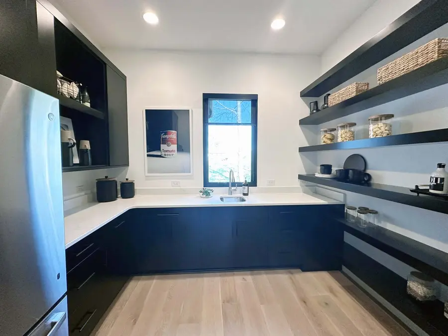 Walk-in pantry with black cabinets, open black shelving and a window over the sink