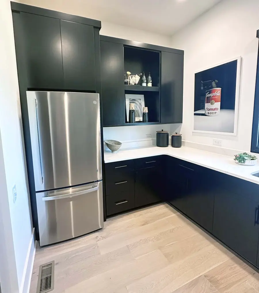 Pantry corner with black cabinets, white countertops and stainless refrigerator