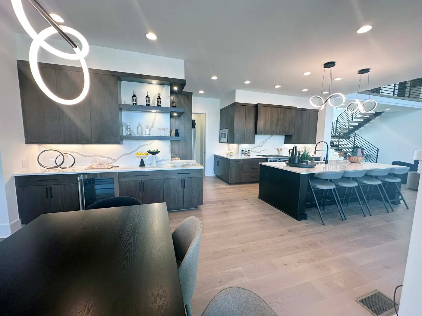 Open kitchen and bar with dark wood cabinets, waterfall-style island and ring pendant lights
