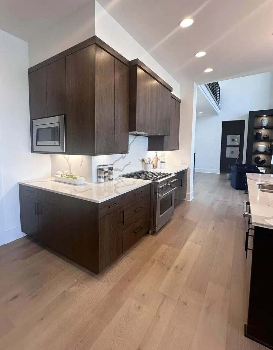 Dark wood kitchen cabinets with built-in microwave, stainless range and marble-look backsplash