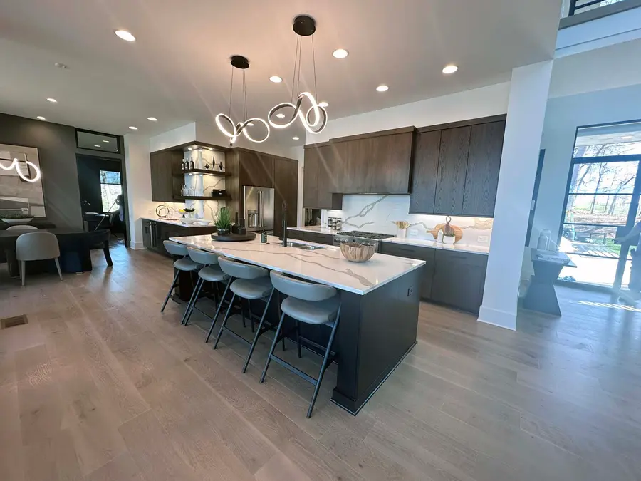 Open kitchen with dark wood cabinets, large island seating five and swirl pendant lights