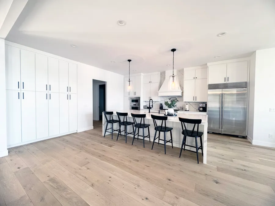 White kitchen with wall of tall cabinets, island with black stools and stainless refrigerator