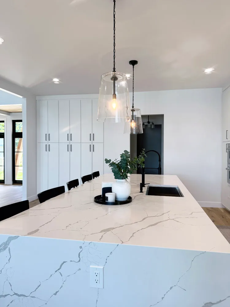 Waterfall marble-look island with black sink and clear glass pendants