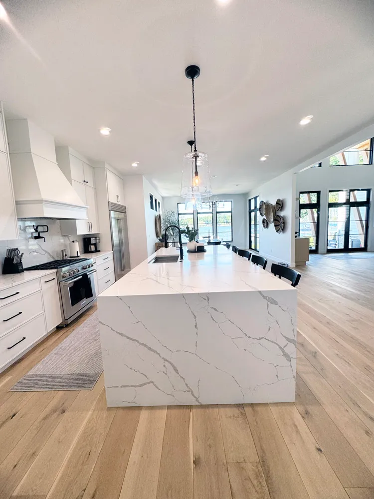Long waterfall marble-look island in a white kitchen open to a bright living area