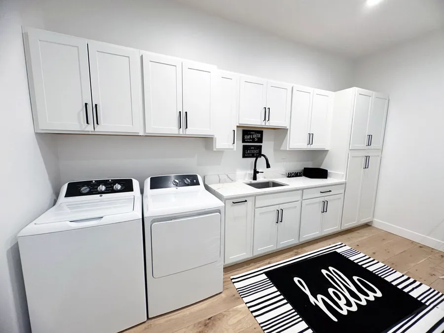 Laundry room with white shaker cabinets, black faucet sink, washer and dryer