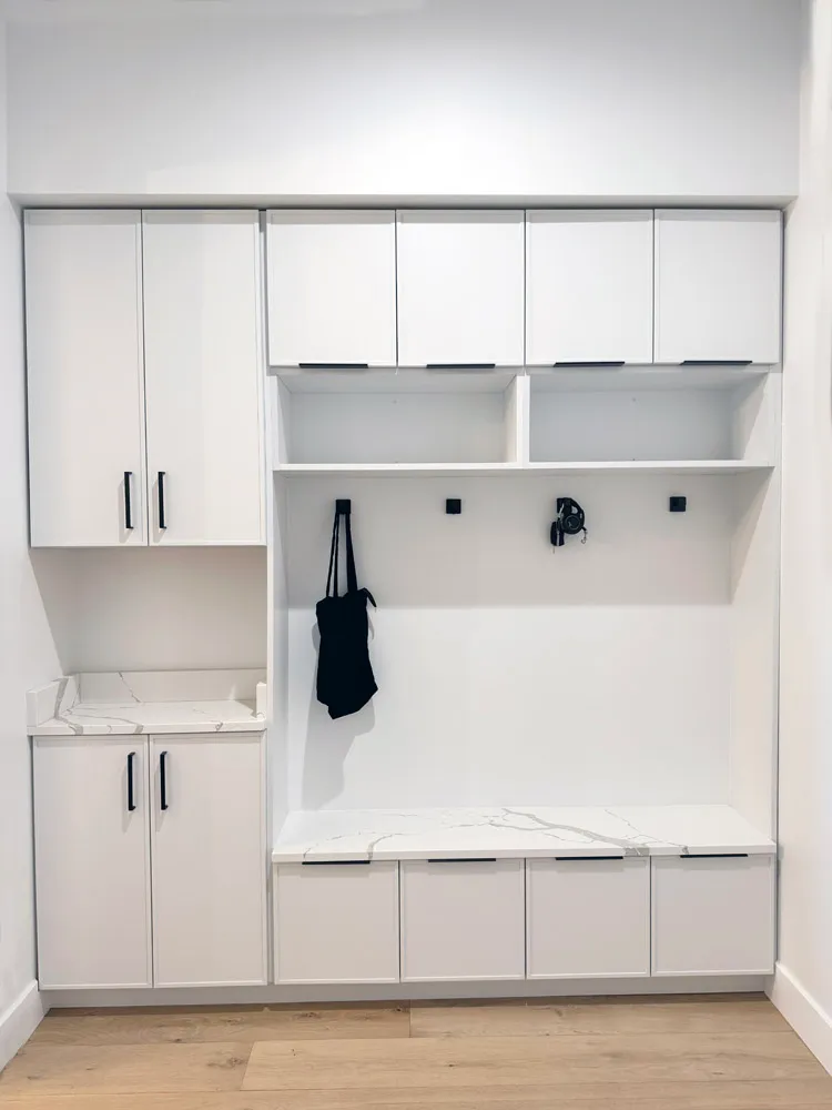 White mudroom built-in with coat hooks, marble-look bench and upper cabinets