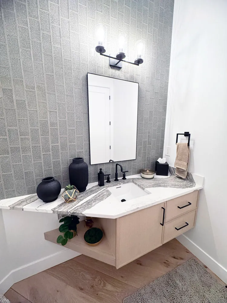 Powder room with floating light wood vanity, veined countertop and gray tile wall
