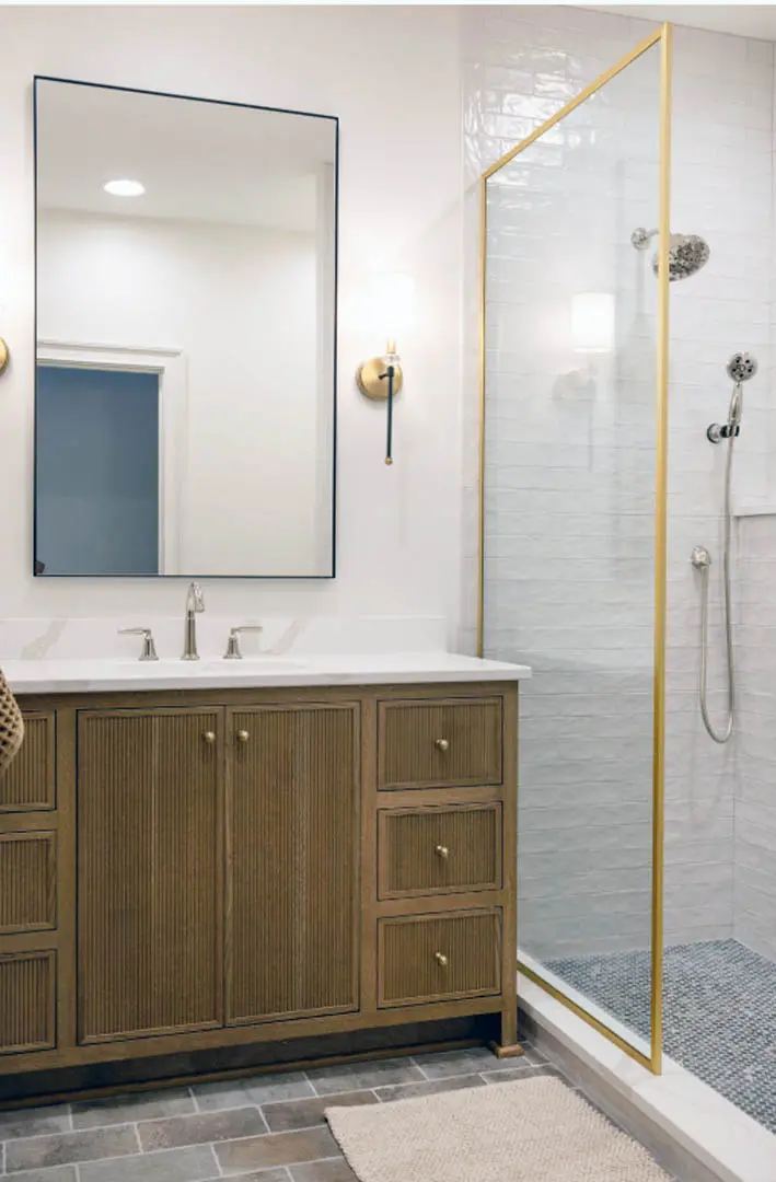 Bathroom with fluted wood vanity, black-framed mirror and brass-framed glass shower