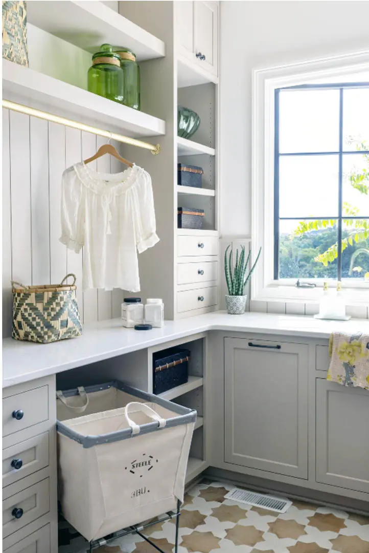 Laundry corner with greige cabinets, hanging rod, open shelves and canvas laundry cart
