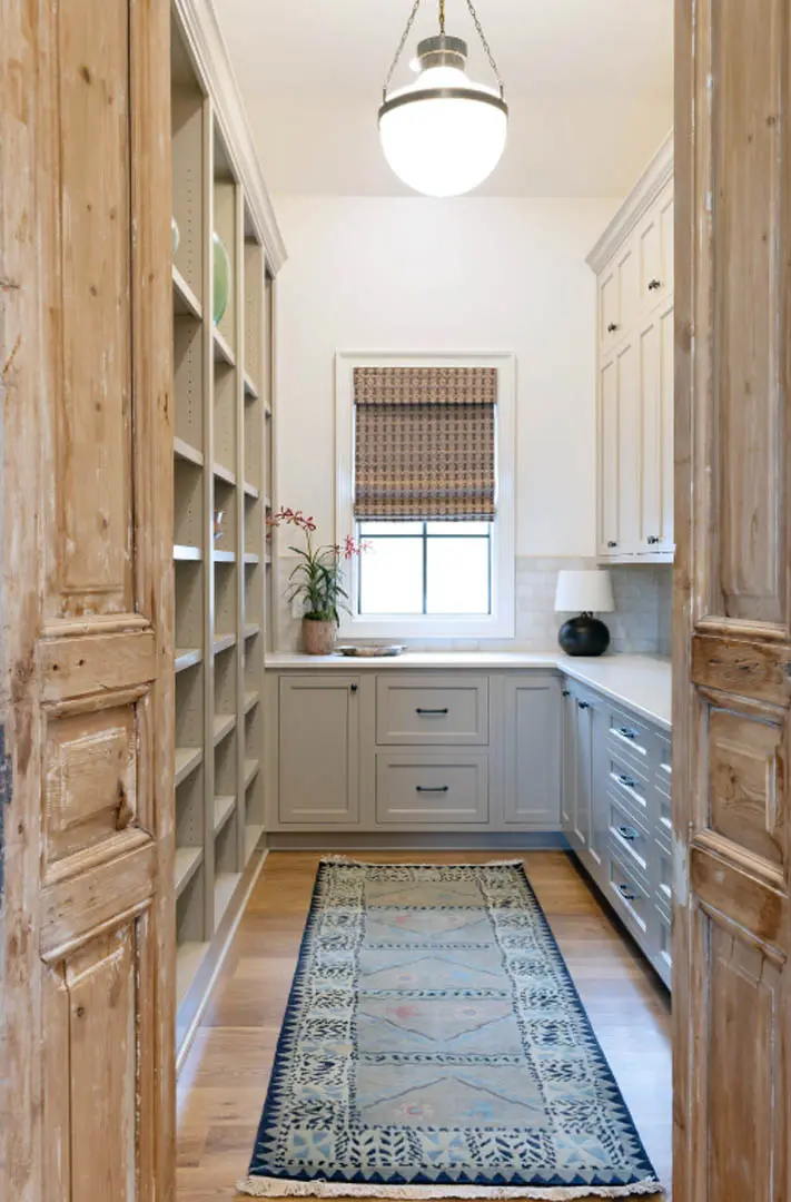 Pantry seen through rustic wood doors with gray cabinets, open shelves and a runner rug