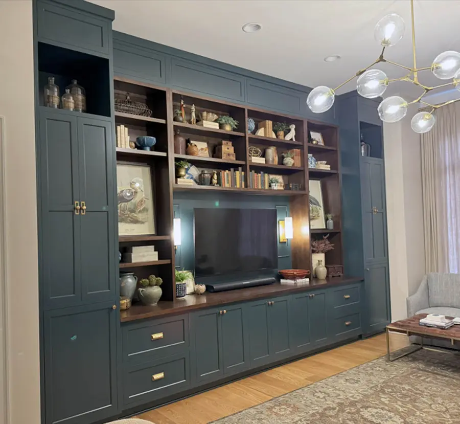 Dark teal built-in wall unit with wood bookshelves around a TV and brass hardware