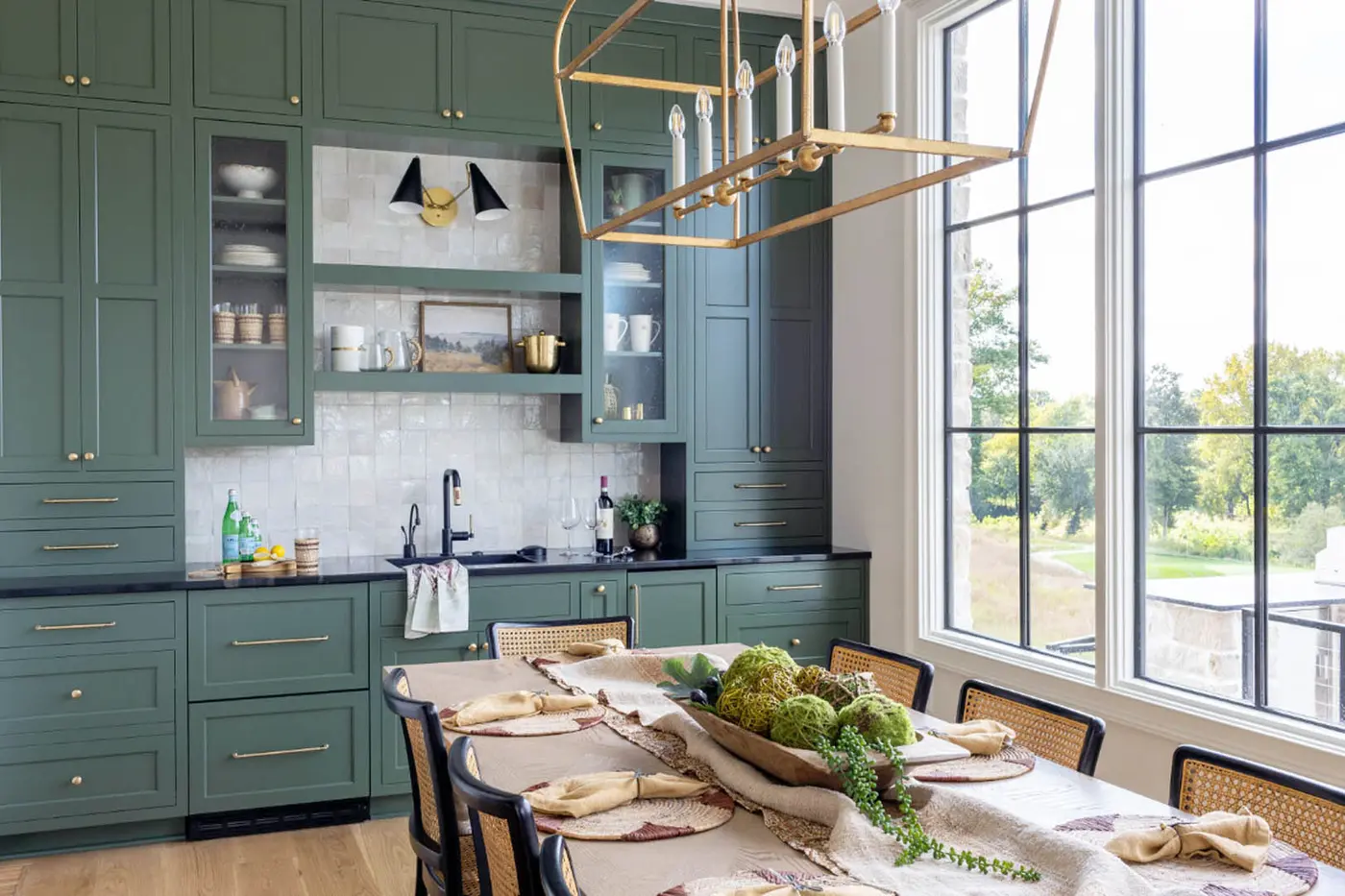 Dining area with green cabinets, open shelves and a black sink beside tall windows