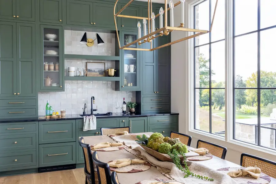 Dining area with green cabinets, open shelves and a black sink beside tall windows