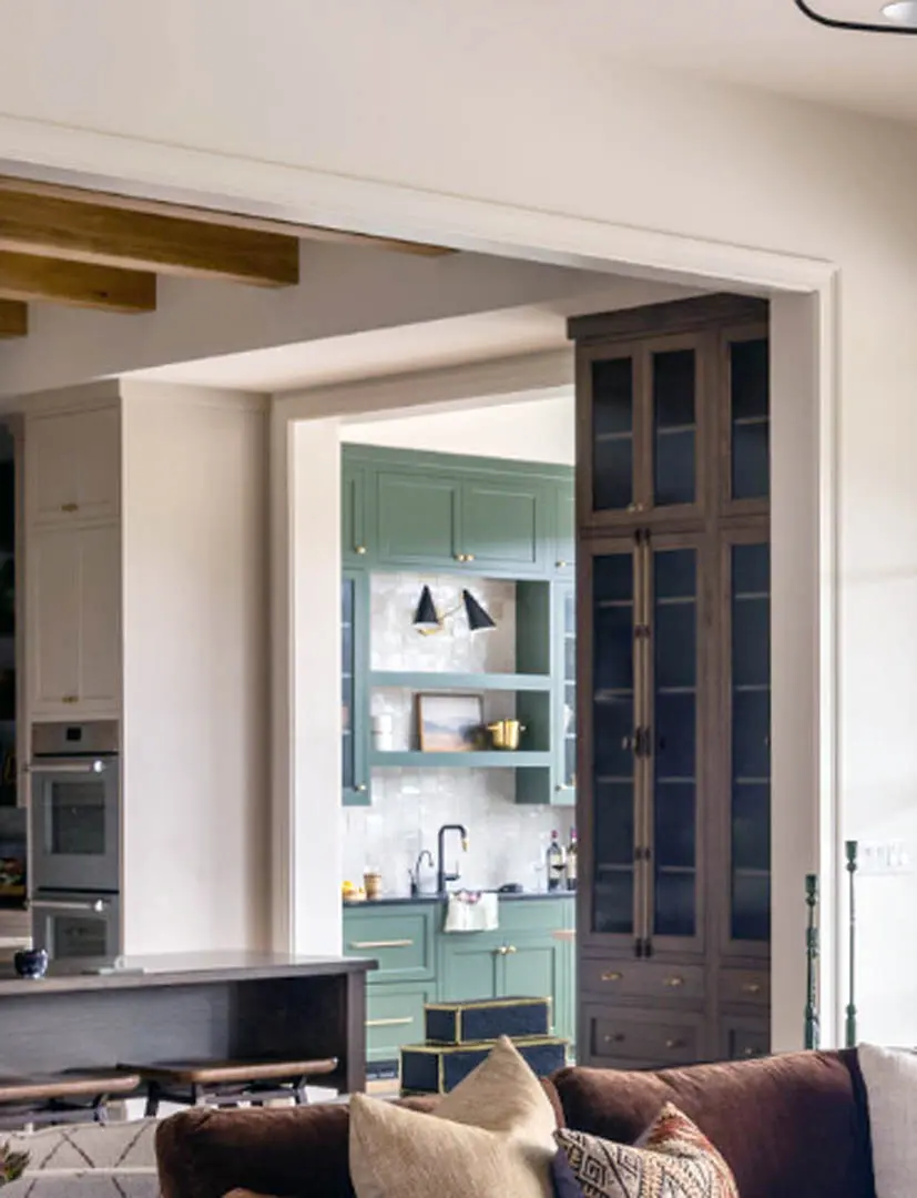 View from living room into kitchen with green cabinet bar and tall glass-front cabinet