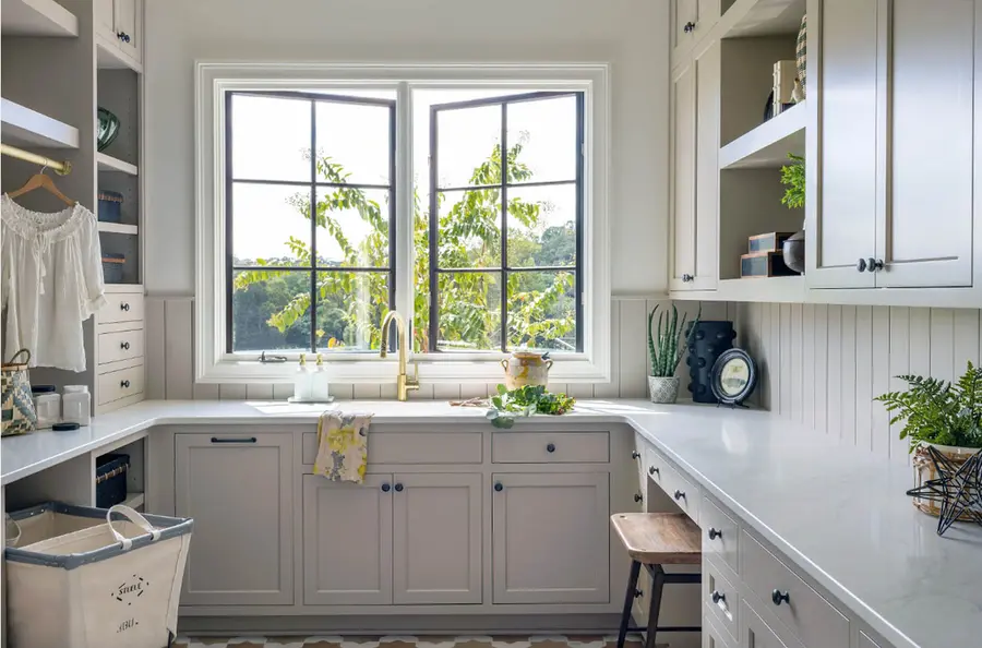 Laundry room with greige cabinets, white counters, brass faucet and black-framed window