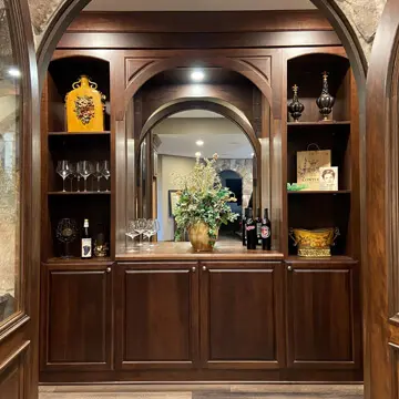Arched dark wood built-in bar with display shelves, mirror and lower cabinets