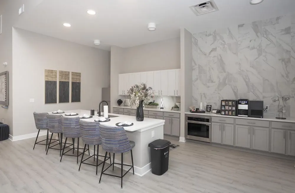 Clubhouse kitchen with white island, upholstered bar stools and gray cabinets
