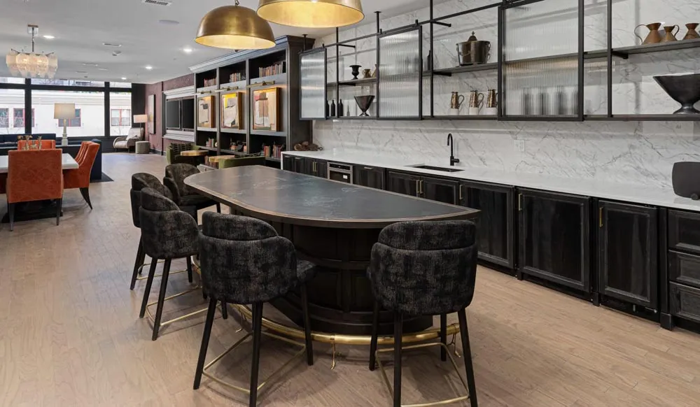 Apartment club room with curved dark island, upholstered stools, black cabinets and brass pendants