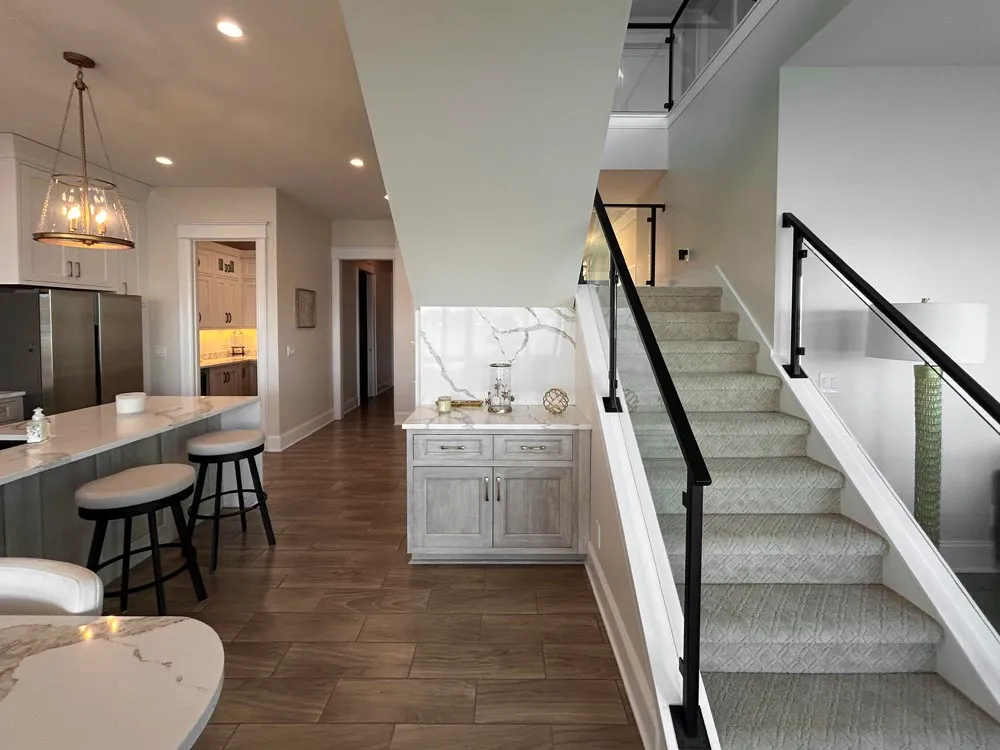 Kitchen island and staircase with black rail beside a gray cabinet and marble backsplash