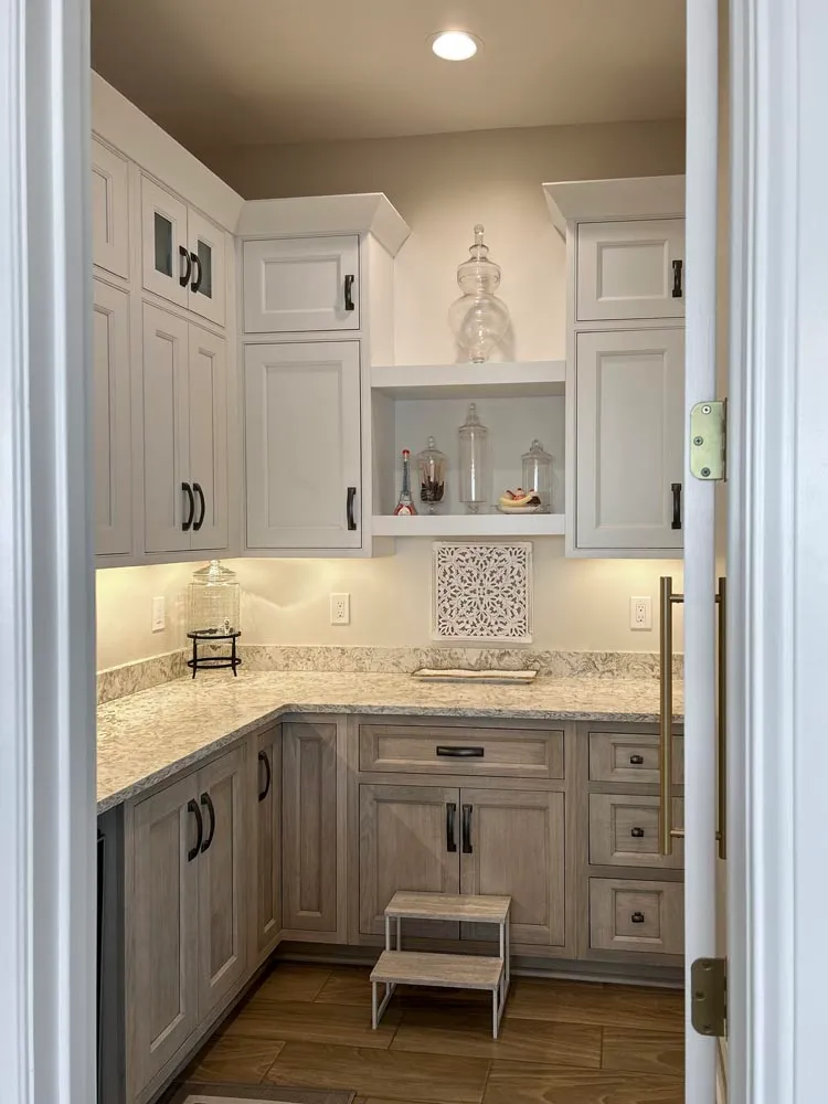 Walk-in pantry with gray-washed base cabinets, white uppers and granite countertops