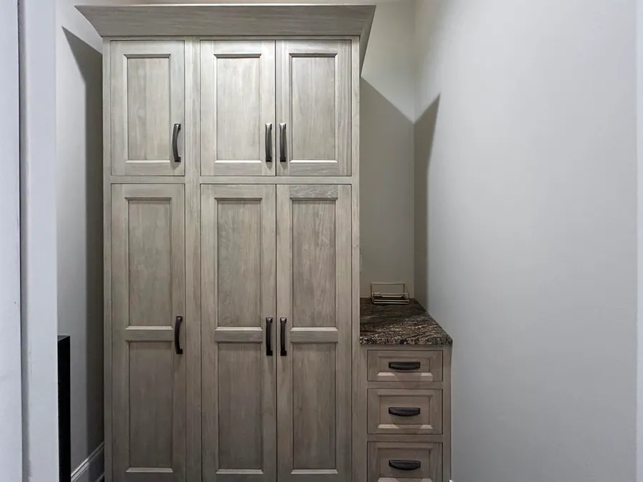 Tall gray-washed pantry cabinet with a small drawer stack and dark granite top