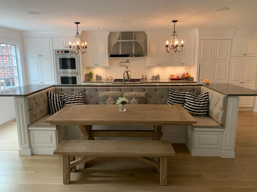 White kitchen island with built-in tufted bench seating around a wood dining table