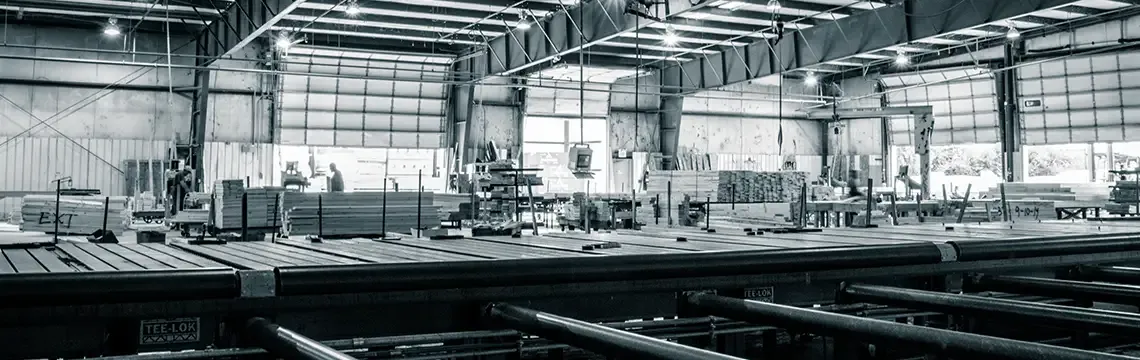 Black-and-white interior of a truss plant with roller conveyors and lumber stacks