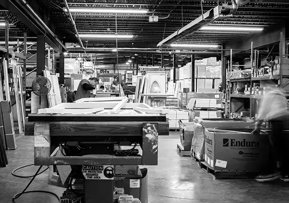 Black-and-white view of a millwork shop with workers assembling door frames