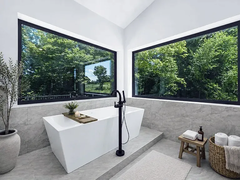Freestanding tub with a black floor-mount faucet between two large corner windows