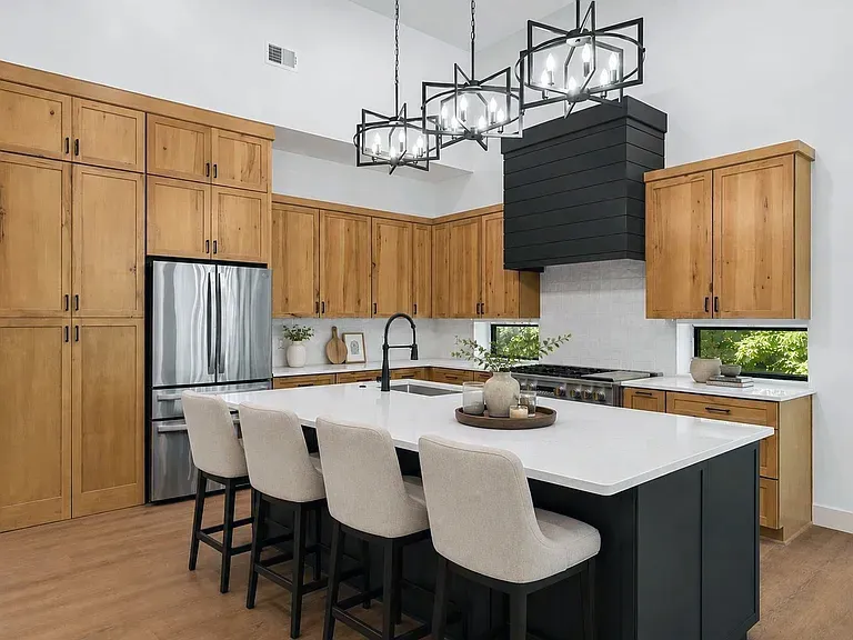 Wood cabinet kitchen with a dark island, white stools, and three black cage chandeliers