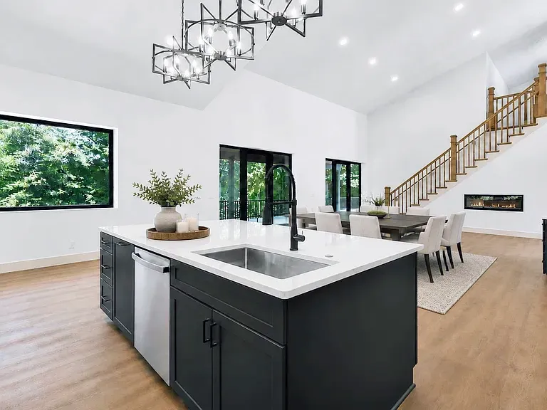 Charcoal island with sink and black faucet overlooking a dining area and staircase