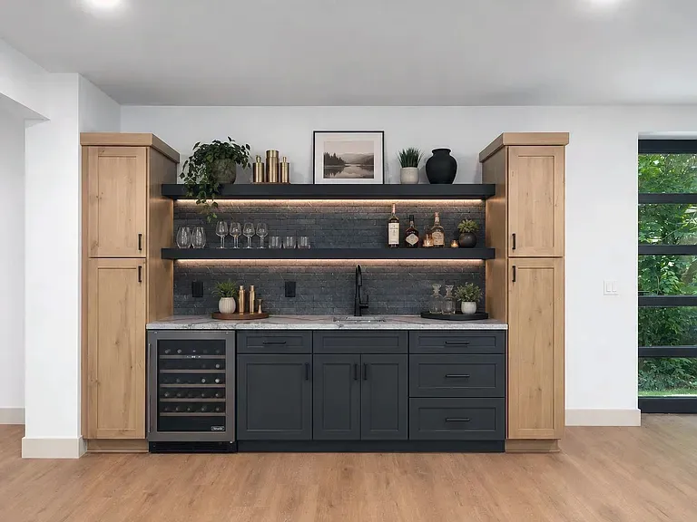 Wet bar with charcoal base cabinets, wood pantry towers, lit floating shelves, and wine fridge