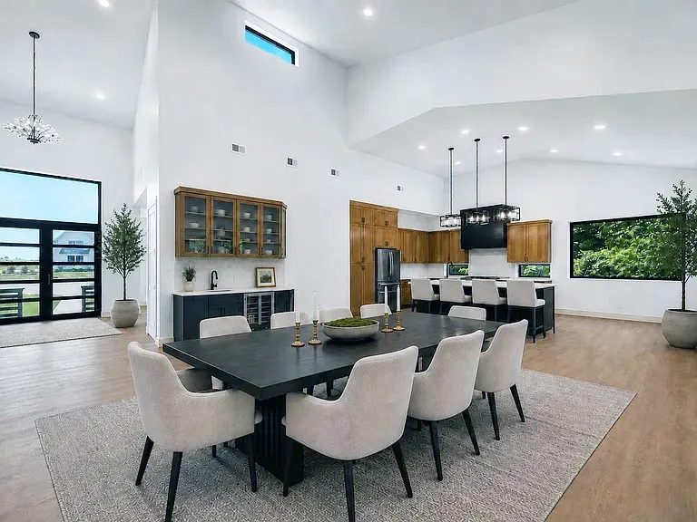 Open great room with a dark dining table facing a wood-cabinet kitchen and bar
