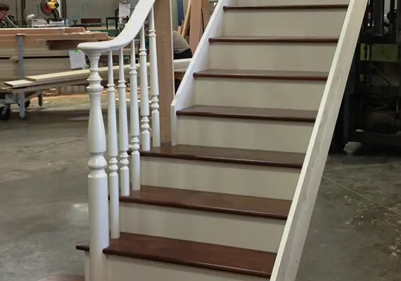 Straight staircase with dark treads and white turned balusters in a millwork shop