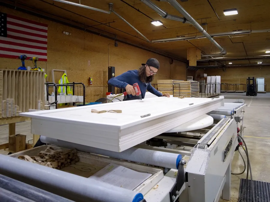 Worker assembling a white prehung door on a machine in a door shop