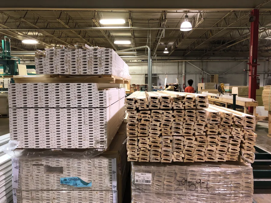 Stacked bundles of primed trim moulding on pallets in a millwork shop