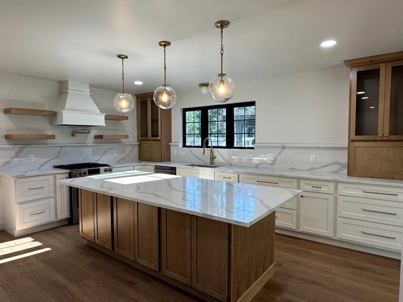 Kitchen with white and wood-tone cabinets, stone island, globe pendants and range hood