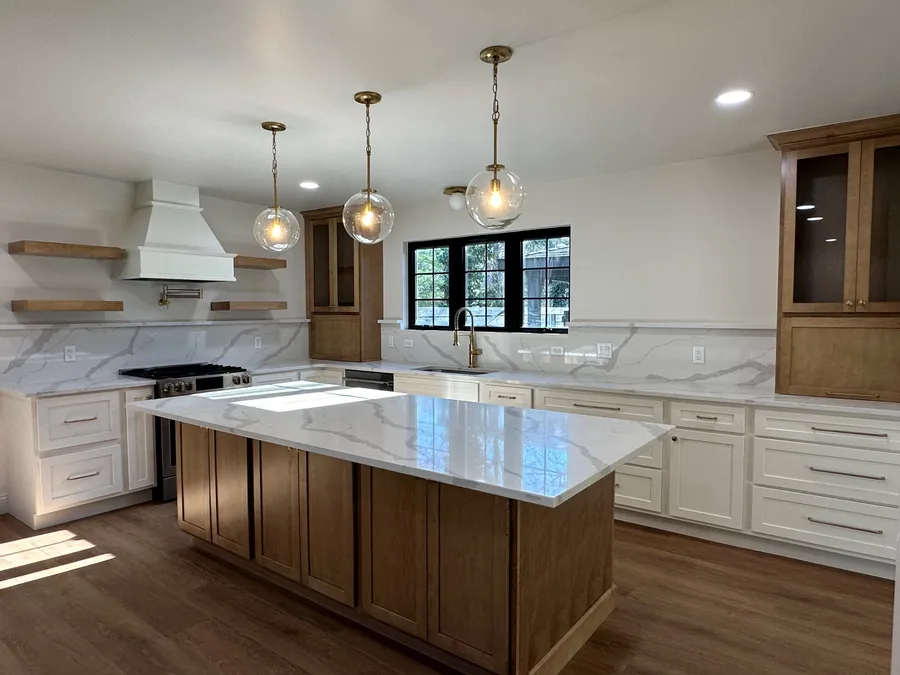Kitchen with white and wood-tone cabinets, stone island, globe pendants and range hood