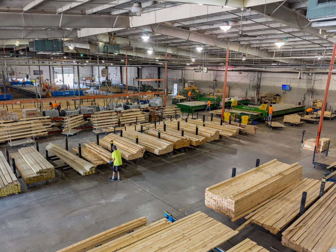Worker among stacks of lumber on carts inside a large manufacturing plant