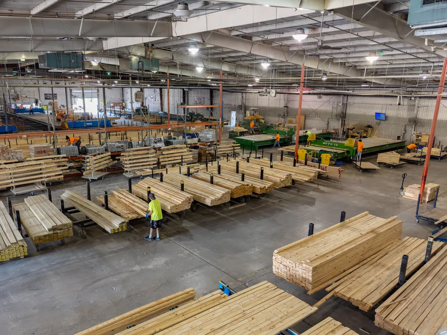 Worker among stacks of lumber on carts inside a large manufacturing plant